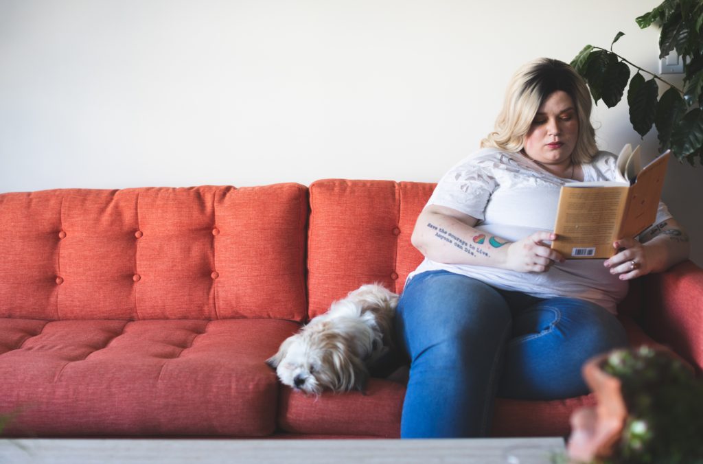 Image of a woman reading while sitting on a orange couch. This type of inactive lifestyle can be a risk factor for diabetes that a functional medicine or holistic doctor in Orland Park & Chicago can help with.