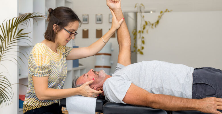 An image of a man laying on a bed as a woman adusts his arm. This could represent how a holistic chiropractor in the Chicago area can offer support with chiropractic care in Orland Park, IL. Learn more about applied kinesiology in Orland Park, IL today.