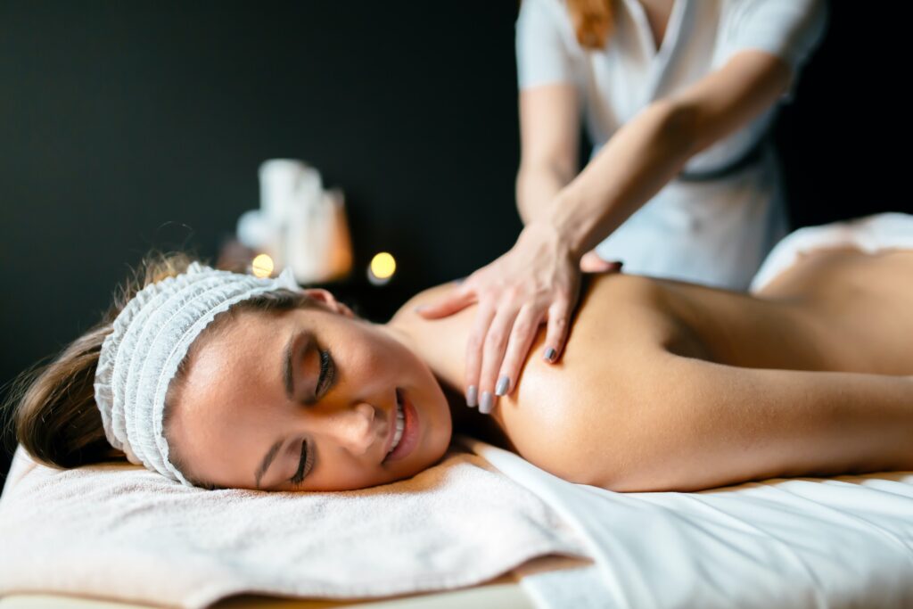 Image of a woman smiling as a massage therapist works on her back. Representing the relaxation that can from prenatal, postpartum, or regular massage therapy in Orland Park, IL.