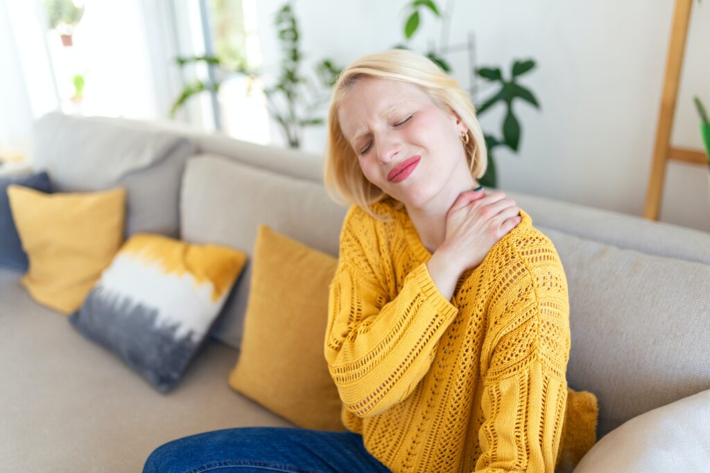 Image of a woman in a yellow sweater grabbing her shoulder. Representing the type of pain a holistic Chiropractor can help with whether in Orland park or in the Chicago area. If you have pain in your shoulder Chiropractic care can help.