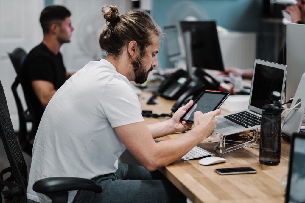 Image of a man sitting at a desk looking at a tablet. Representing 2 of the 5 reasons to see a Chiropractor in Orland Park or the Chicago area. Chiropractic care can help address pain from sitting and looking at screens.