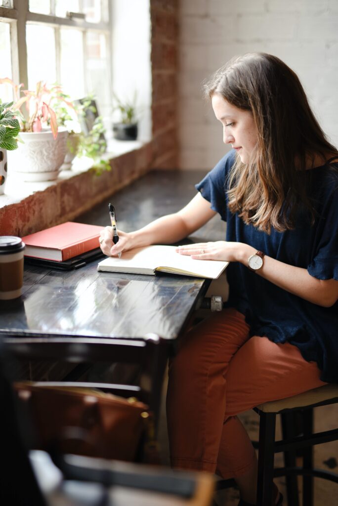 Image of a woman in a blue shirt writing in a journal. Showing the importance of keeping a headache diary to show your holistic chiropractor in the Chicago area. It can also be helpful when seeking acupuncture or functional medicine in Orland Park, IL.