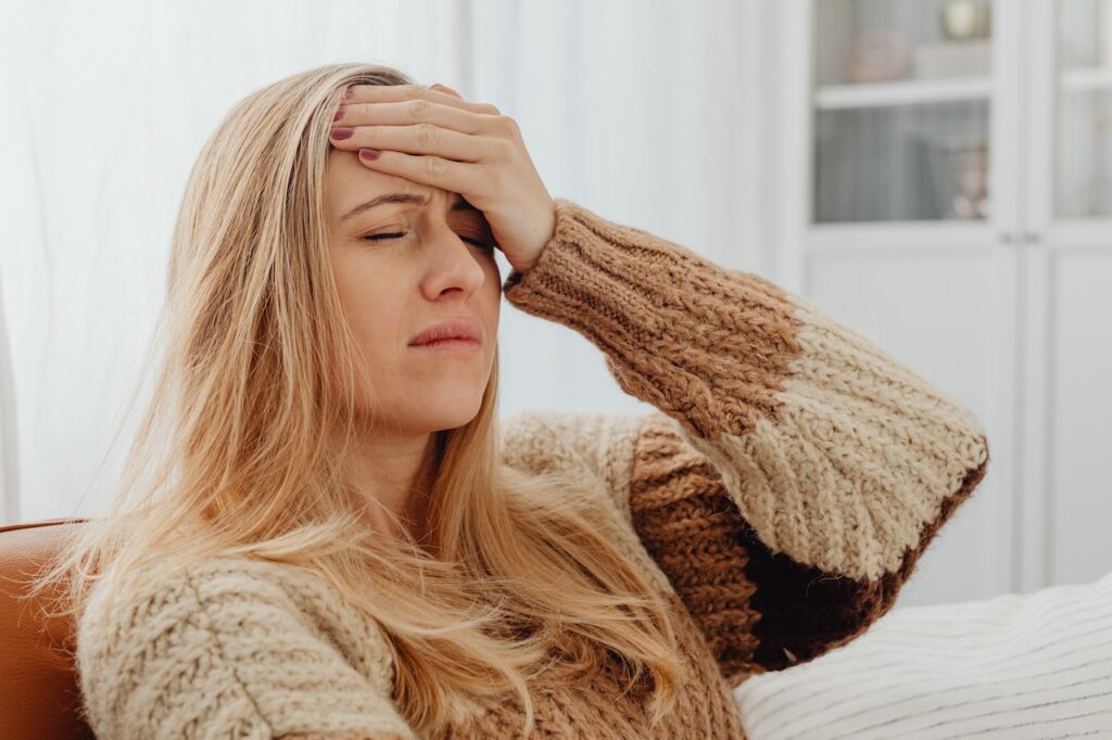 Image of a woman in a brown sweater holding her head. Representing what it feels like to have a headache which can be treated with chiropractic care. Or by a acupuncturist or holistic doctor in Orland Park, IL. 