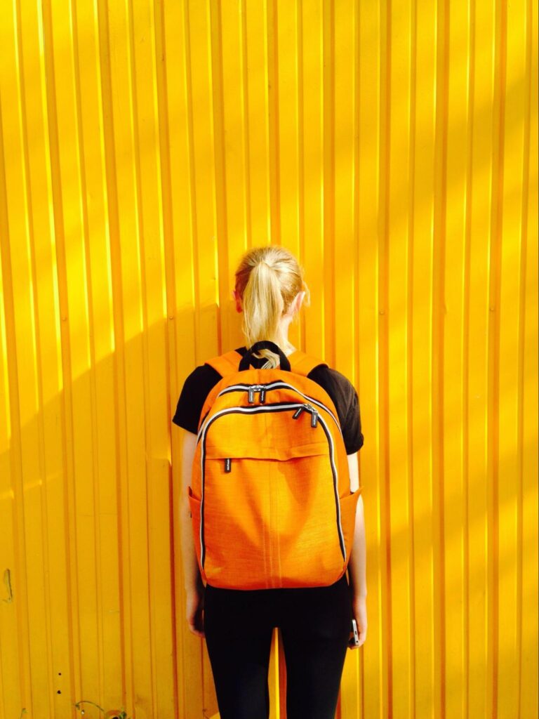 A child wearing a backpack stands facing a yellow wall. Learn how chiropractic care in Orland Park, IL can offer support by searching for "chiropractor orland park" today. Chiropractic care for sciatica in orland park, IL can help your child and the new school year. 
