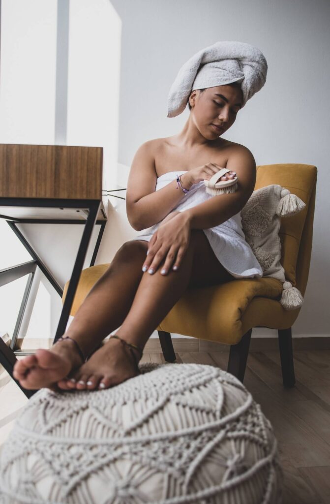 A woman brushes her arm while wrapped in a towel. This could represent the benefits of massage therapy in Orland Park, IL. Learn more from a holistic doctor in Orland Park, IL or contact a massage therapist in Orland Park, IL. 
