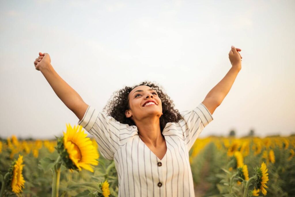 A smiling woman raises her hands while standing in a sunflower field. This could represent the benefits of improved mental health through functional medicine in Orland Park, IL. Search for a functional medicine doctor in Orland Park, IL.
