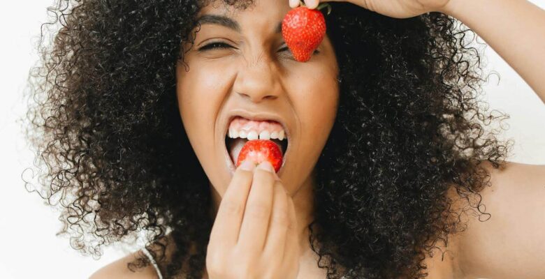A woman looks at the camera with her mouth open, about to bite into a strawberry while holding another in front of her left eye. Learn how certain foods can help you cope with PCOS by contacting an acupuncturist in Orland Park, IL or searching for acupuncture in Orland Park, IL today.