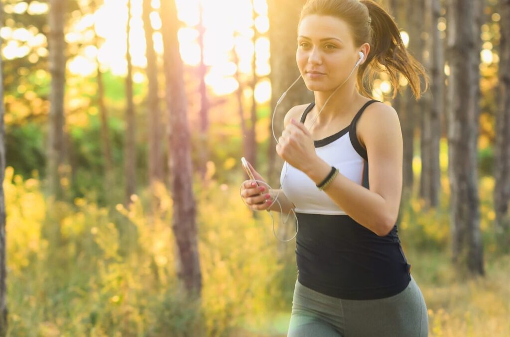 A woman smiles while running though a forest while listening to music. This could represent the benefits of exercise for lowering inflammation. Contact a holistic doctor in Orland Park, IL to learn more about holistic acupuncture Orland Park, IL and other services.
