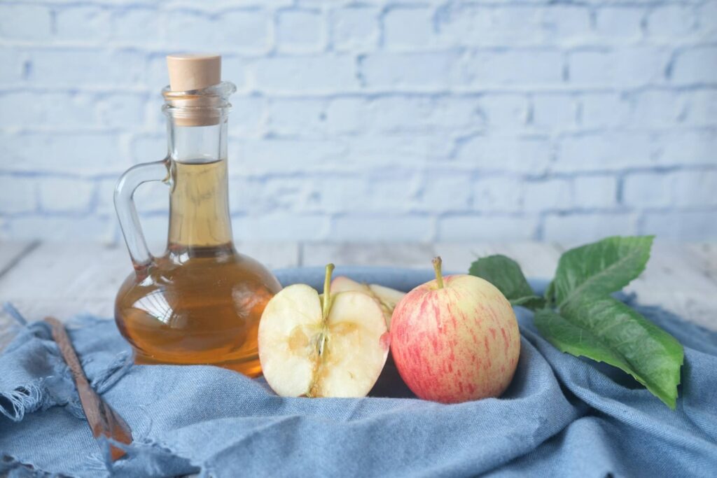 An apple cut in half rests next to a bottle of apple cider vinegar, which can help lower blood sugar. Learn more about addressing blood sugar issues with Shape Reclaimed in the Chicago area. Search for a holistic doctor in Orland Park, IL to learn more.
