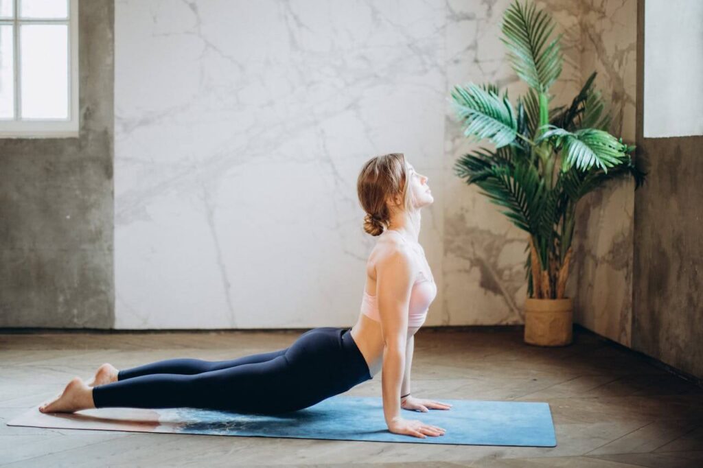 A woman on a yoga mat stretches in a pose while looking out a window. Learn how to help support your posture by contacting a holistic chiropractor in the Chicago area. Search for a holistic massage in Orland Park, IL to learn more about things like chiropractic care in Orland Park, IL. 
