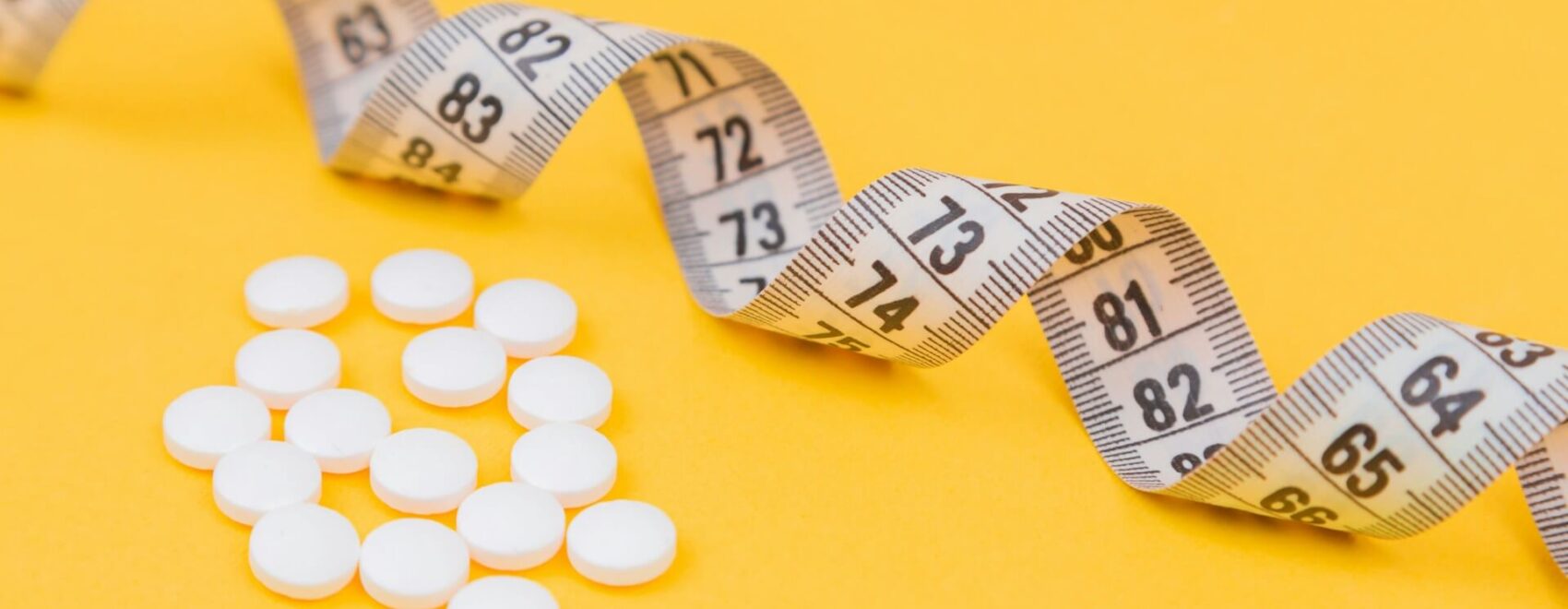 A close up of a measuring tape and pills against a yellow background. Learn how Shape ReClaimed in the Chicago area can offer an alternative to GLP-1 injections. Search for a holistic doctor in Orland Park, IL to learn more.