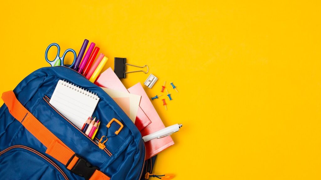 A close up image of a students backpack with school supplies including paper, pens, and scissors. Learn more about overcoming back to school stress by working with a massage therapist in Orland Park, IL. Search for massage therapy in Orland Park, IL or massage therapy near me today. 
