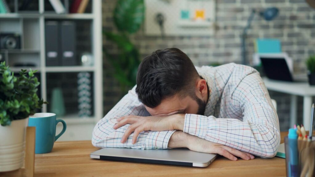 A man sits at a desk with their head down, resting on their laptop. This could represent the lack of energy as a part of long COVID that functional medicine in Orland Park, IL can help address. Learn more about holistic medicine in the Chicago area and how a functional medicine doctor in Orland Park, IL can help. 
