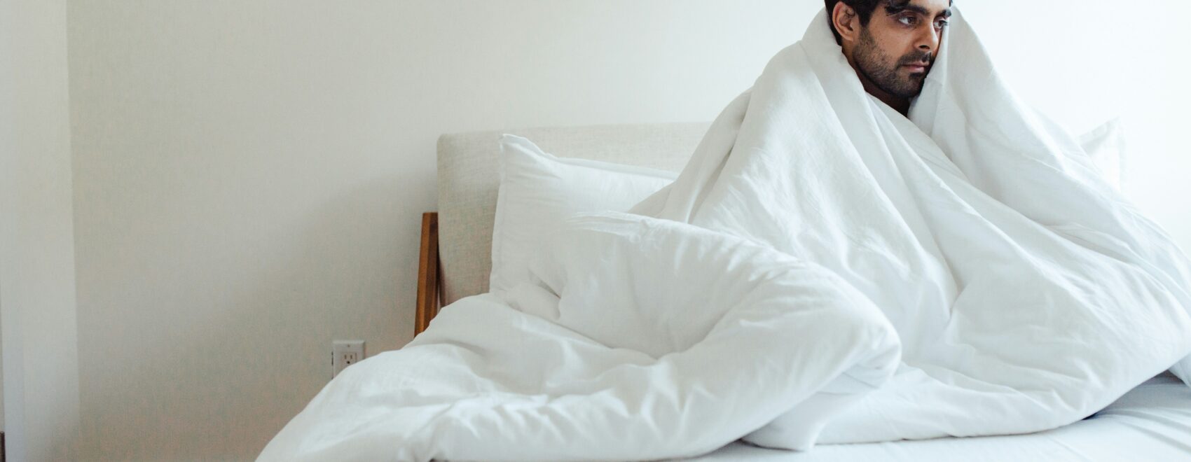 A man sits on a bed covered with a blanket. Learn how functional medicine in Orland Park, IL can help you recover from covid by searching for a holistic doctor in Orland Park, IL. They can offer support with "what is functional medicine chicago area" and more.