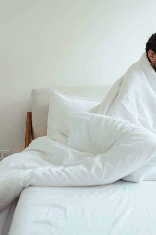 A man sits on a bed covered with a blanket. Learn how functional medicine in Orland Park, IL can help you recover from covid by searching for a holistic doctor in Orland Park, IL. They can offer support with "what is functional medicine chicago area" and more.