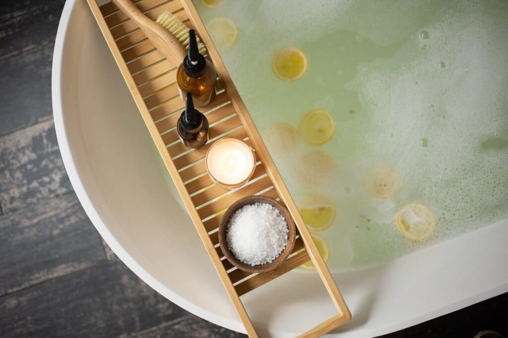 A top down view of a bowl of salt, candle, and oils resting above a tub filled with water and lemon slices. Learn more about how epsom salt baths can help assist detoxification in Orland Park, IL by searching for shape reclaimed in the chicago area today.
