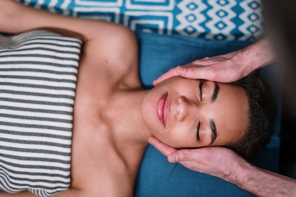 A woman with medium skin tone is lying down with her eyes closed, receiving a soothing face massage. Learn how a therapeutic massage in Orland Park, IL can offer support with promoting oxytocin naturally. Search for massage Chicago area to learn more about how a holistic doctor in Chicago, IL can help. 
