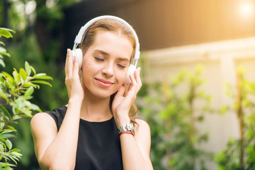 A young woman with light brown hair is wearing white headphones and smiling peacefully while listening to music. This could represent how music can help boost oxytocin. Search for a massage therapist in Orland Park, IL to learn more about how a holistic massage in Orland Park, IL can help. 
