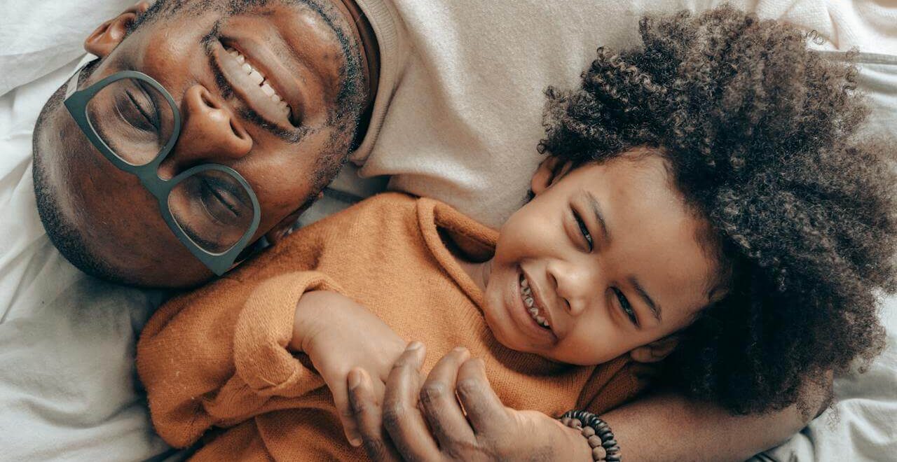 A top down view of a smiling father playing with their child. This could represent the benefits of seeking a therapeutic massage in Orland Park, IL. Search for a massage therapist in Orland Park, IL to learn more about how a holistic massage in Orland Park, IL can help promote oxytocin.