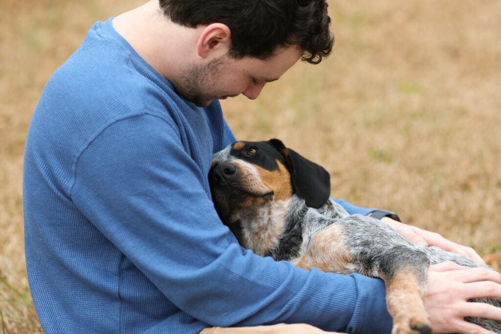 A young man in a blue sweater is sitting on a grassy field, holding his black and tan dog close while gazing into its eyes affectionately. The dog looks back lovingly. Search for how pets can help boost oxytocin by contacting a holistic doctor in Chicago, IL today. They can offer massage therapy in Orland Park, IL and more.
