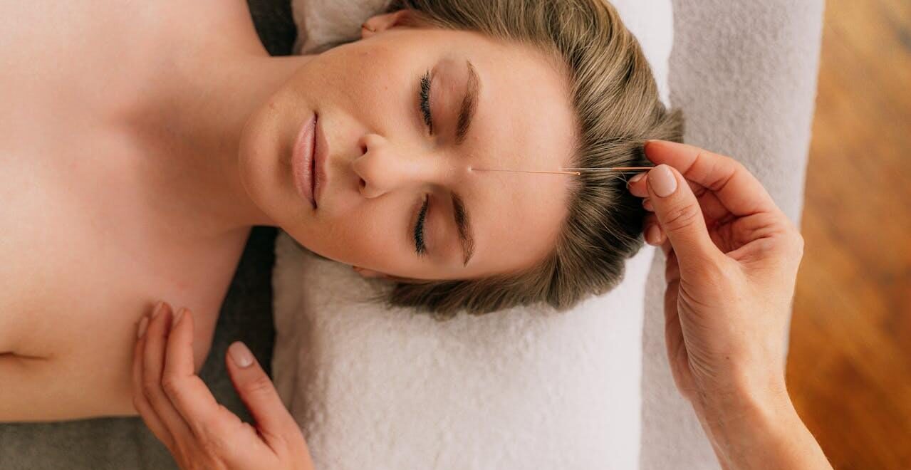 Shows a woman laying on a pillow with an acupuncturist in Orland Park, IL standing here. Represents how acupuncture in Orland Park, IL can support you on your fertility journey.