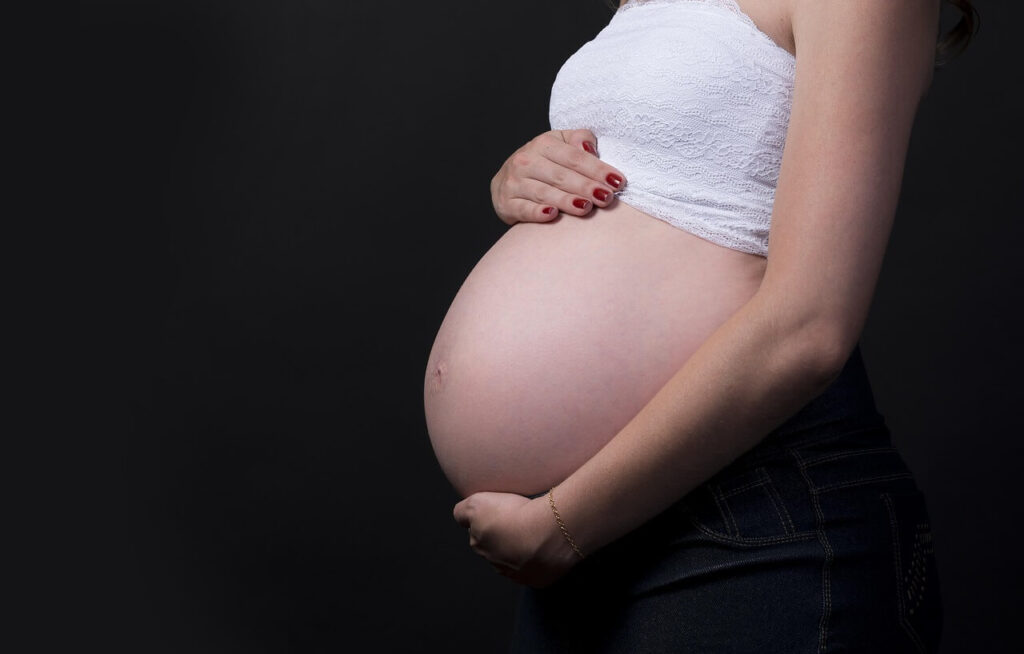 Pregnancy Photo | functional medicine doctor in the chicago area | holistic chiropractor in the chicago area | holistic doctor in chicago, il | chiropractic care in orland park, il | Gold Coast | Streeterville | River North Shows a mother with a cropped white shirt, holding her pregnant stomach. Represents how finding the best care from a holistic chiropractor in the chicago area can help with the day to day of pregnancy with help from chiropractic care in orland park, il.