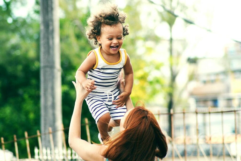 Shows a month tossing her smiling child in the air. Represents how a holistic chiropractor in the chicago area can support children throughout their childhood with chiropractic care in orland park, il.