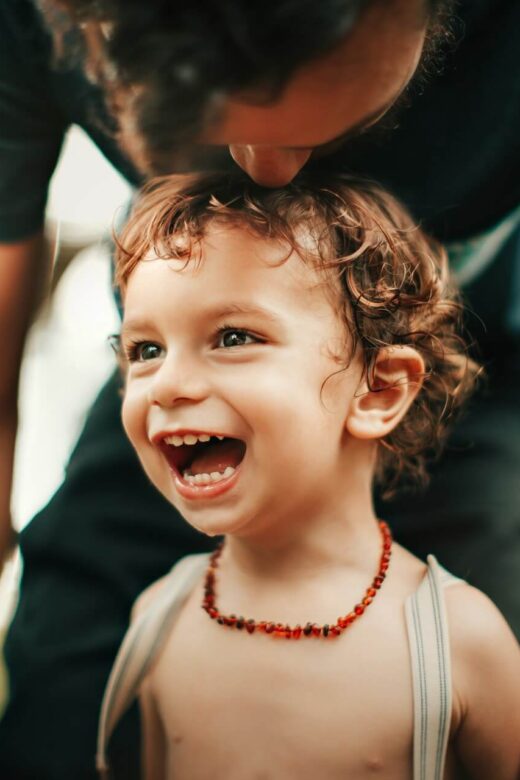 Shows a child with a big smile with their parent kissing their head. Represents how a chiropractor orland park or a holistic chiropractor in the chicago area can help your child while they grow.