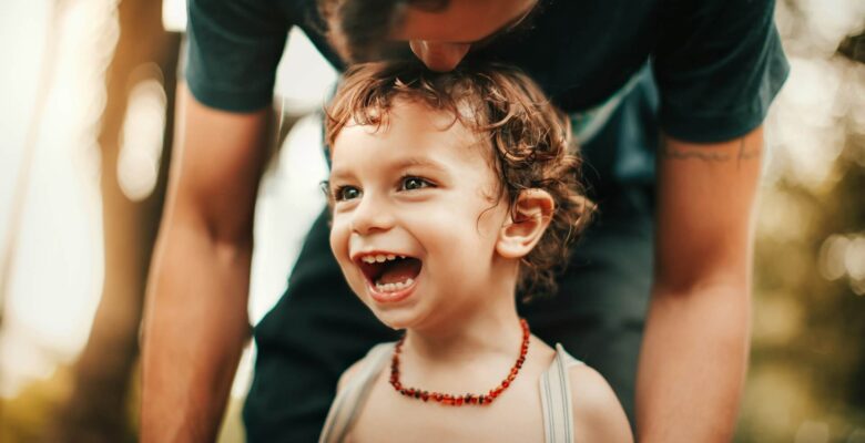 Shows a child with a big smile with their parent kissing their head. Represents how a chiropractor orland park or a holistic chiropractor in the chicago area can help your child while they grow.