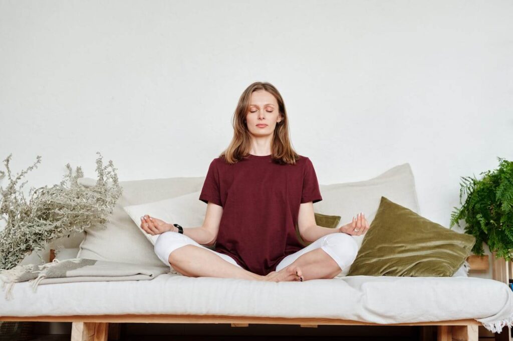 Woman sitting peacefully on a couch with her eyes closed meditating. Learn to ease your stress and support your blood sugar balance with the help of a functional medicine doctor in Orland Park, IL.