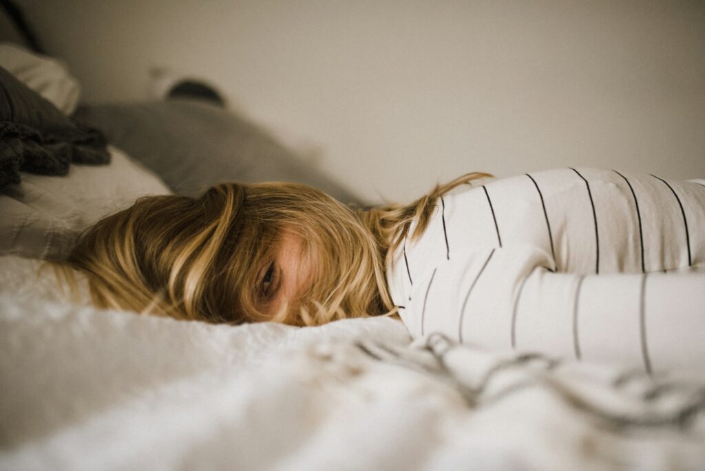 Tired woman laying on her stomach in bed with her hair covering her face. Learn to overcome out of sync cortisol rhythm with the help of a functional medicine doctor in Orland Park, IL.