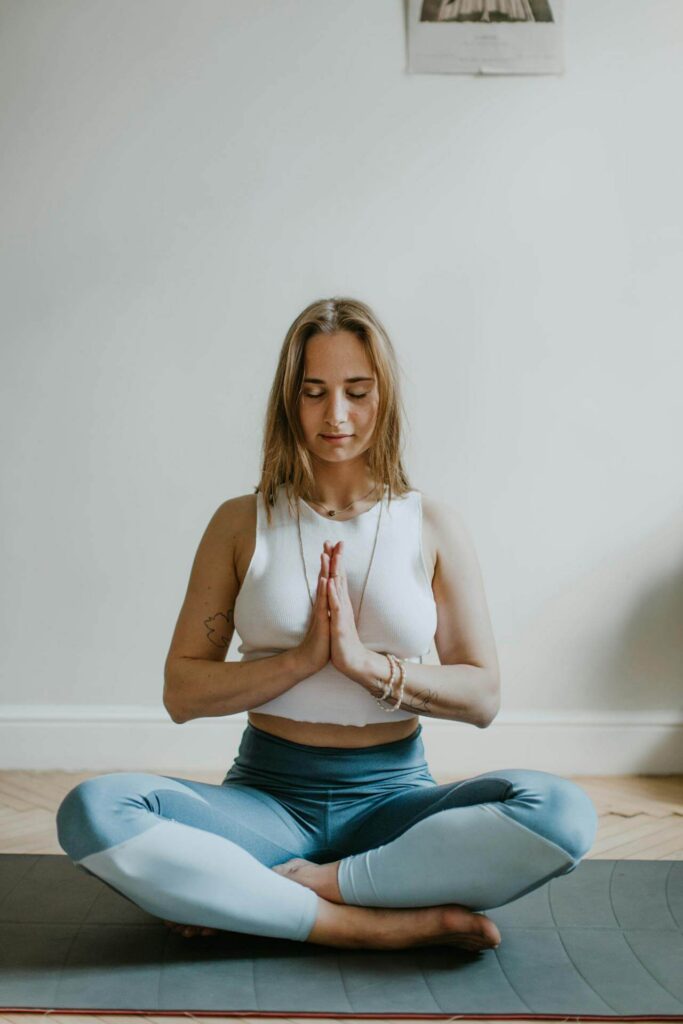 Woman sitting cross legged on a yoga mat with her eyes closed. Manage your stress and adrenal fatigue in healthy ways with a functional medicine doctor in Orland Park, IL.