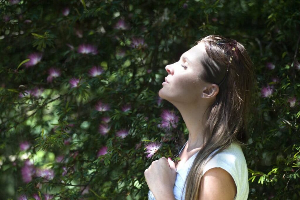 Peaceful woman standing outside with her eyes closed with a green grassy wall behind her with purple flowers. Look deeper into your mood issues with the support of functional medicine in Orland Park, IL and see how blood sugar is affecting it.