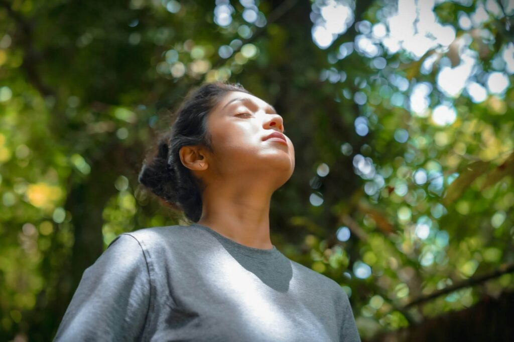 Peaceful woman standing in a forest with her eyes closed facing the sky. Tired of feeling overwhelmed? A functional medicine doctor in Orland Park, IL can help you find answers.