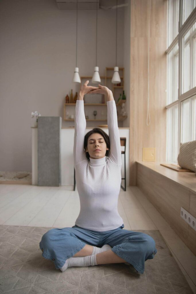 Woman sitting on the floor cross legged stretching her arms above her head. Functional medicine in Orland Park, IL takes a whole-body approach to stress, fatigue, and burnout.