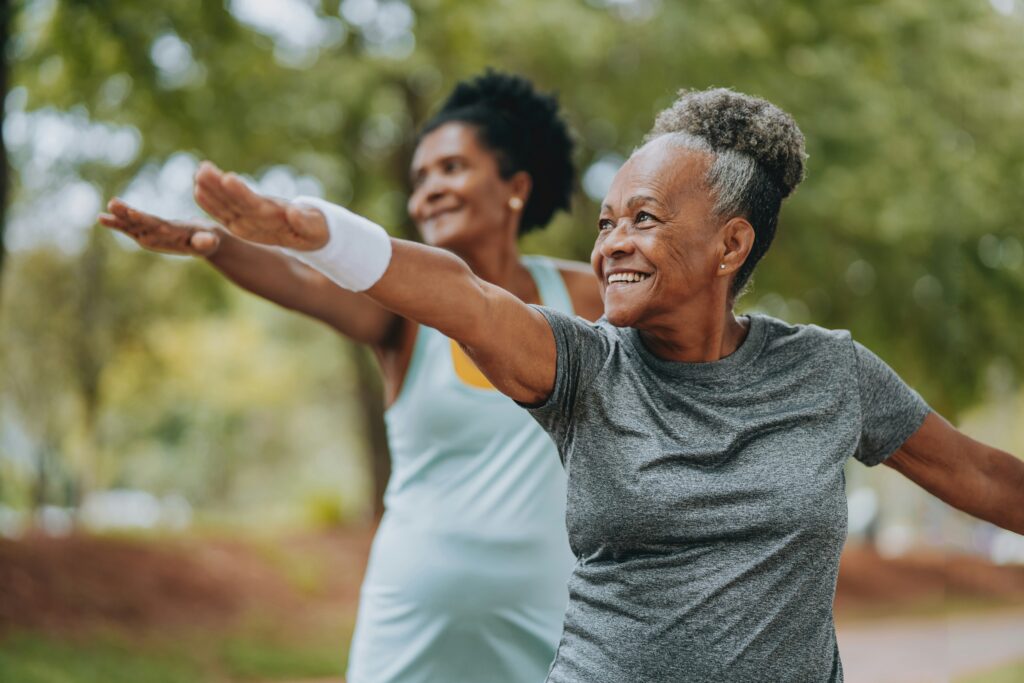 Two older women standing in a park smiling while practicing yoga.  Take back your health and start healing with the support of a functional medicine doctor in Orland Park, IL. 
