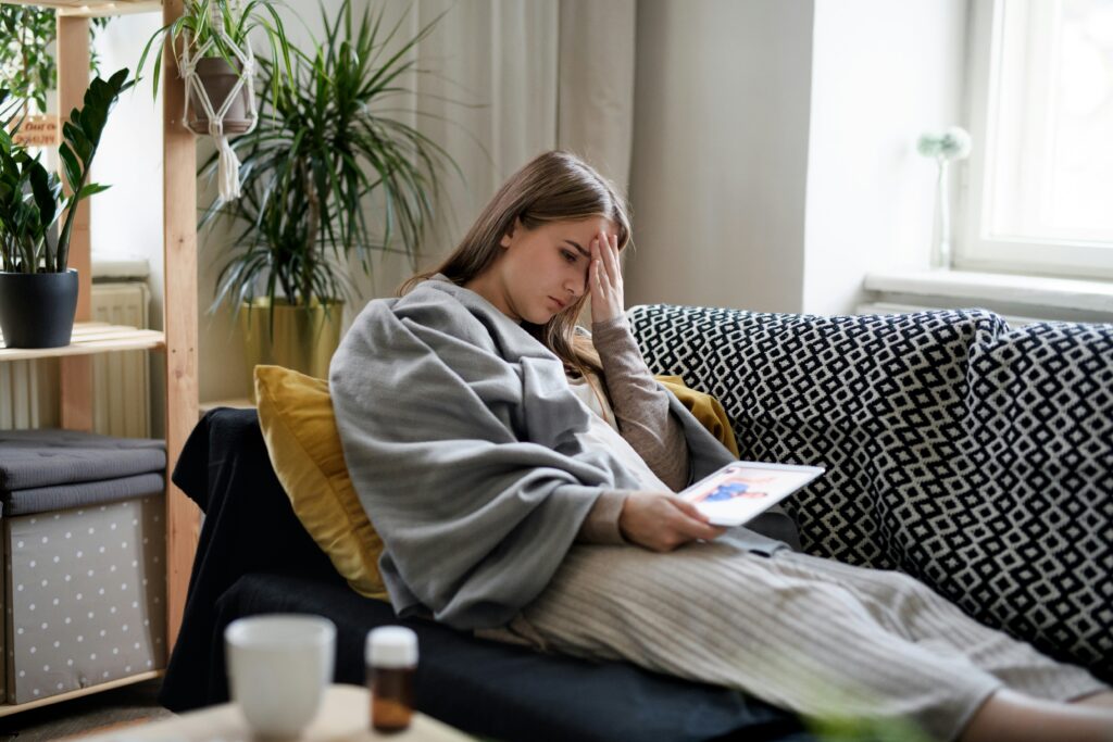 Girl sitting on a couch placing a hand on her forehead with a tired expression. Discover how functional medicine in Orland Park, IL can help you take back control of your health.