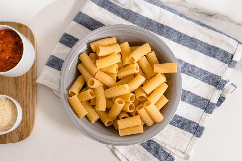 pasta | functional medicine in Orland Park, IL | functional medicine sleep | blood sugar and mood | Orland Park | Tinley Park | Frankfort Bowl full of raw pasta on a striped towel. Learn what foods to avoid to help with fatigue with the support of functional medicine in Orland Park, IL.