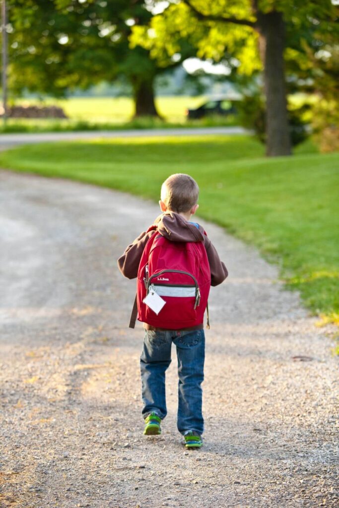 red backpack | functional medicine insomnia | sleep support | functional medicine in Orland Park, IL | Frankfort | Mokena | Tinley Park Little boy walking down a gravel path carrying a red backpack. Functional medicine insomnia support helps kids and parents reset sleep routines and feel their best heading into the school year.