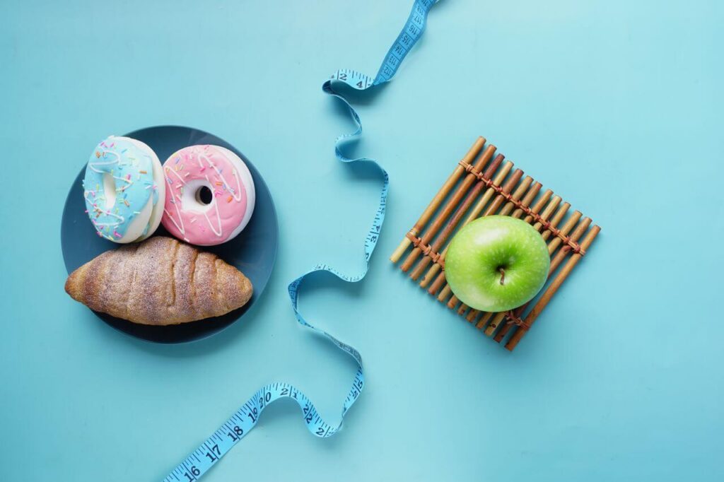 Plate of donuts next to a green apple and measuring tape. Learn to support your blood sugar balance for sustainable weight loss with shape reclaimed in Orland Park, IL.