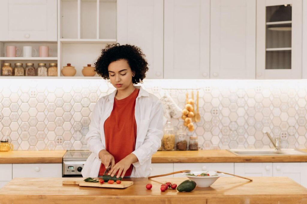 Woman standing in a kitchen cutting a cucumber on a wooden cutting board. Discover how blood sugar swings and insulin affect your body and how Shape Reclaimed in Orland Park, IL can help with weight loss.
