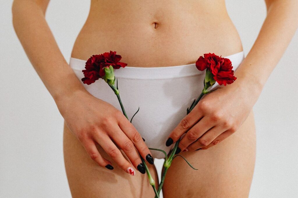 Woman in white underwear holding two red carnations. With the support of a functional medicine doctor in Orland Park, IL you can begin to manage your PMOS symptoms in healthy ways.