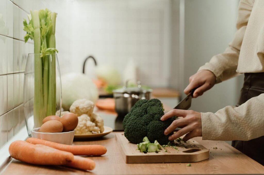Woman holding a knife chopping up broccoli on a wooden cutting board. Get root cause support for your PMOS with functional medicine in Orland Park, IL.