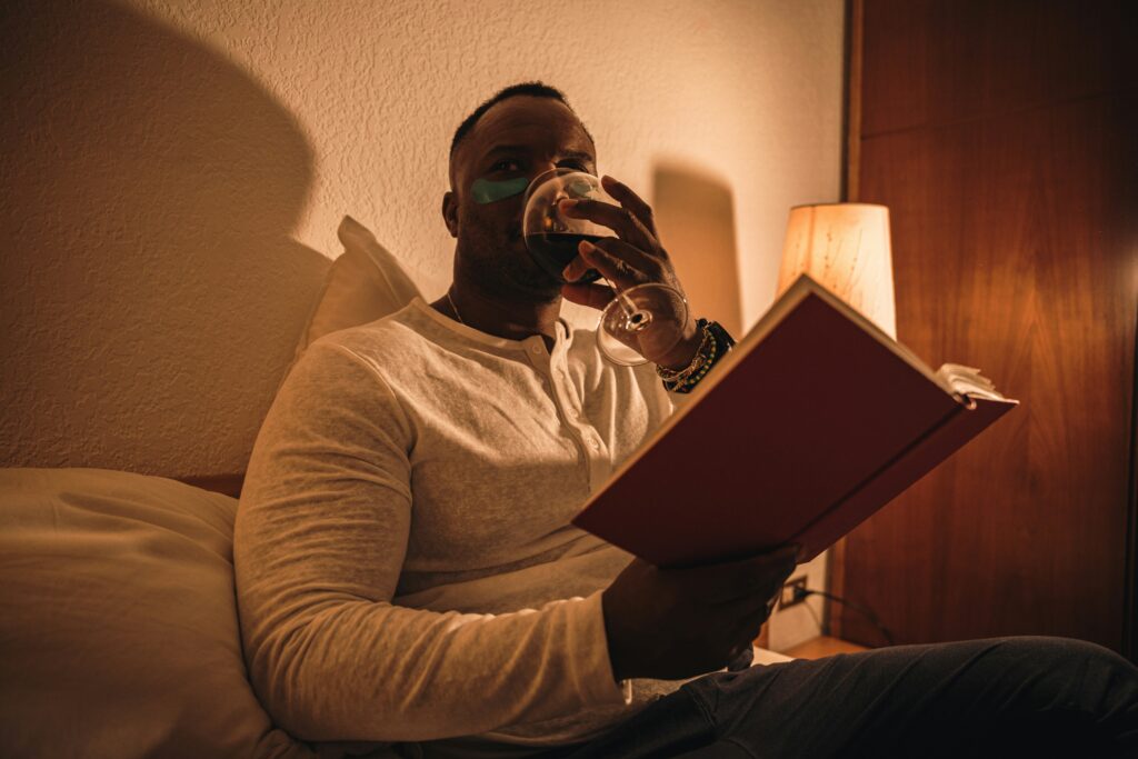 Man drinking red wine while in bed reading in Orland Park IL