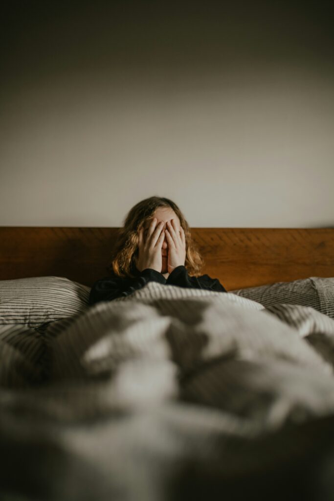 Woman sitting up in bed frustrated that she is waking up at 3am in Orland Park IL not able to sleep. 