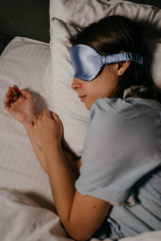 Woman laying in bed wearing a blue sleep mask. Support your hormone balance with the help of functional medicine in Orland Park, IL.