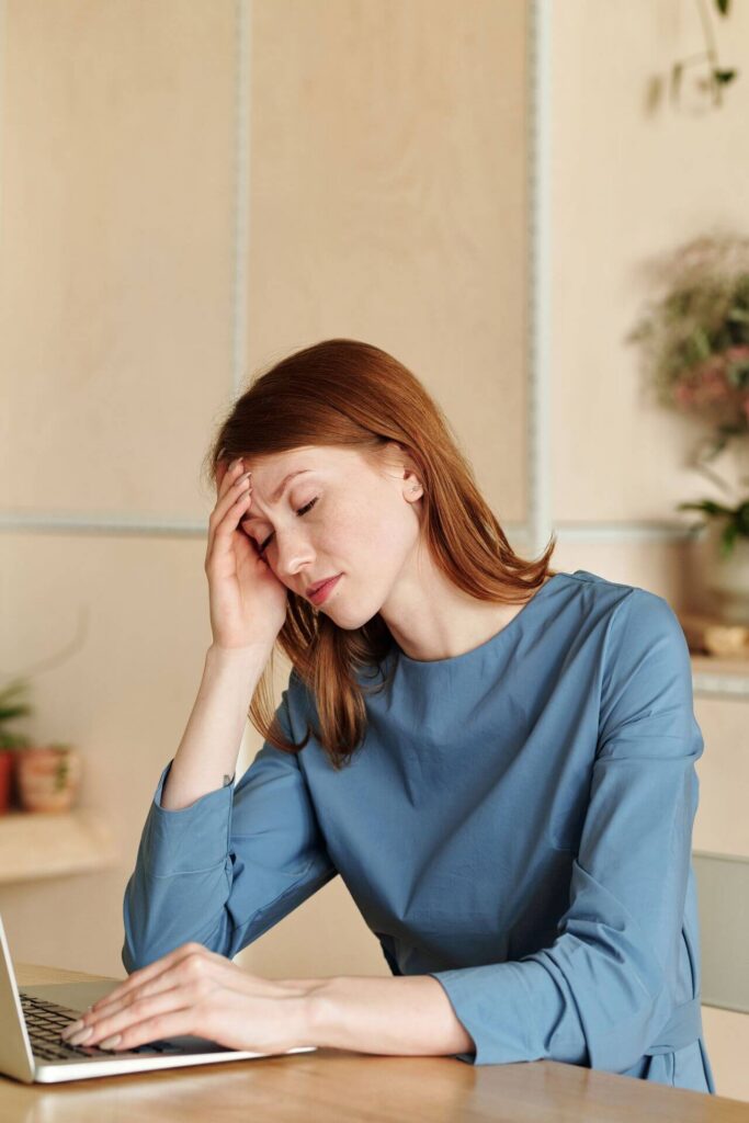 Tired woman sitting at a counter in front of a laptop. Heal your low t symptoms with the help of a supportive functional medicine in Orland Park, IL.